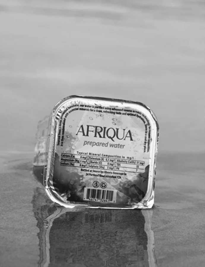 A single sealed Afriqua cup on a reflective beach, in black and white