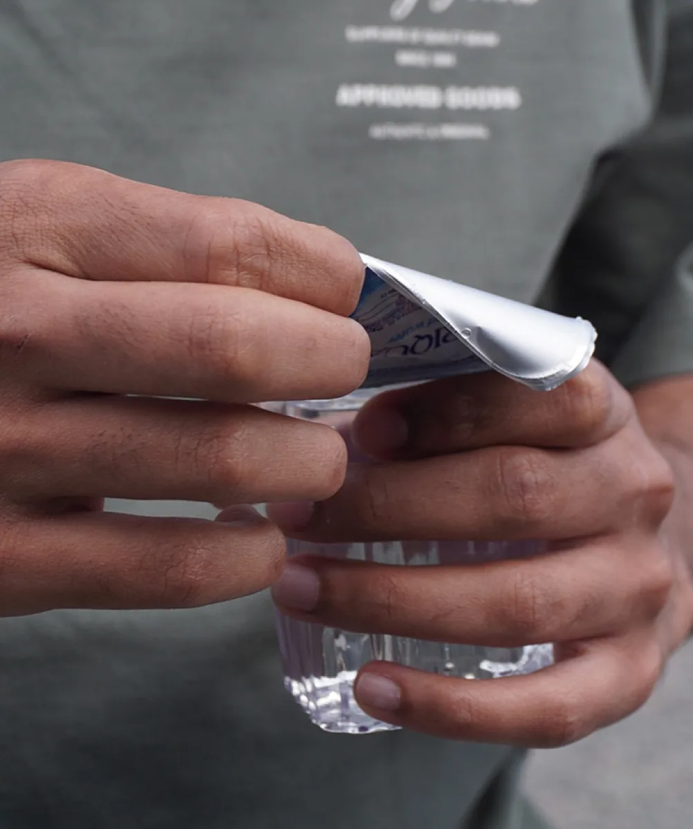 Hands peeling the foil seal from an Afriqua 200 ml water cup